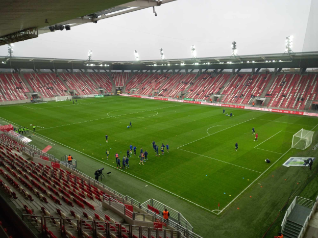Ein Fußballfeld in einem Stadion mit Zuschauern drumherum unter Stadionbeleuchtung, mit dem Himmel im Hintergrund.