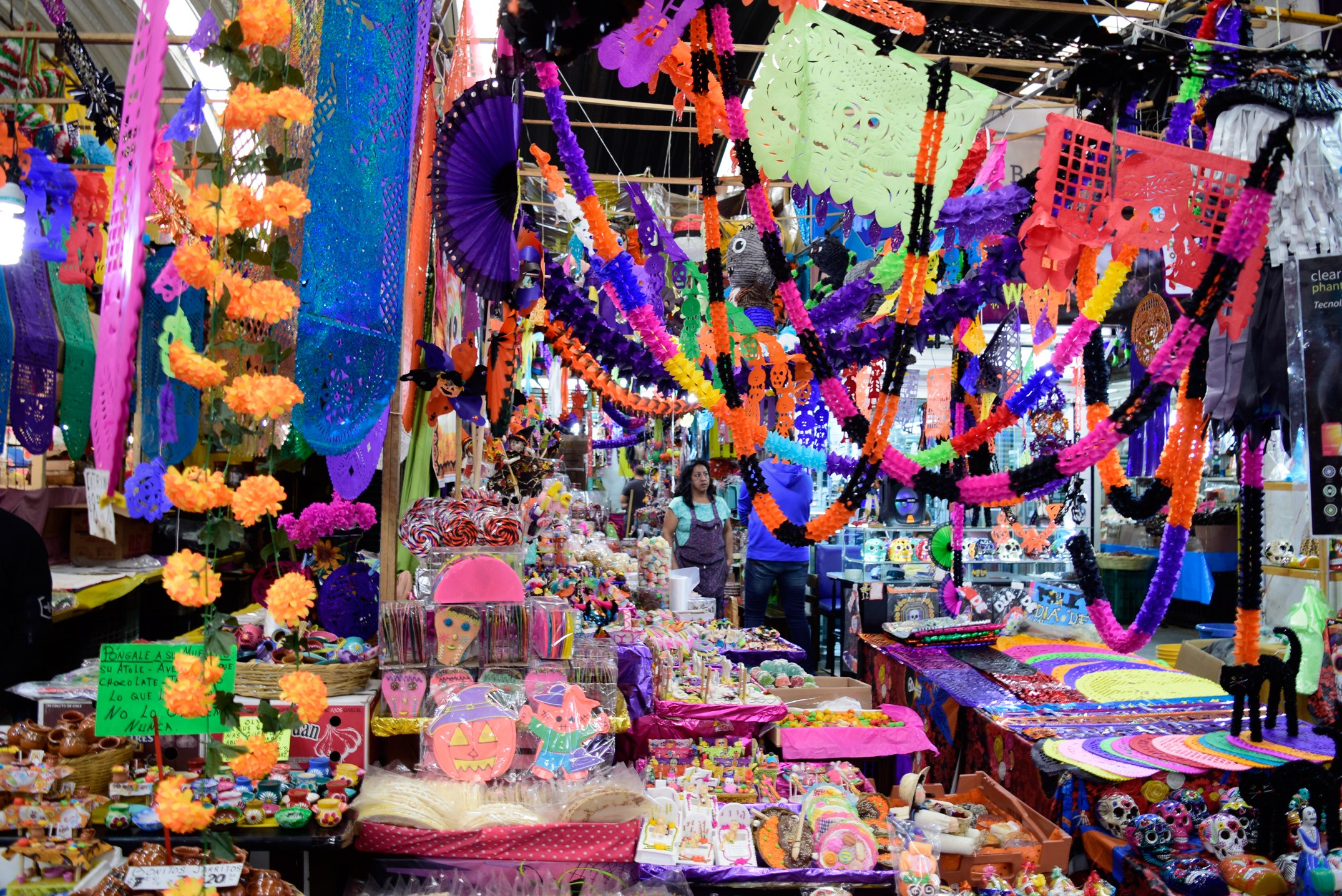 Ein belebter Markt mit Ständen, die Spielzeug, Dekorationsgegenstände und andere Gegenstände verkaufen, unter einer Decke, die mit Lichtern geschmückt ist, mit Menschen, die herumlaufen.