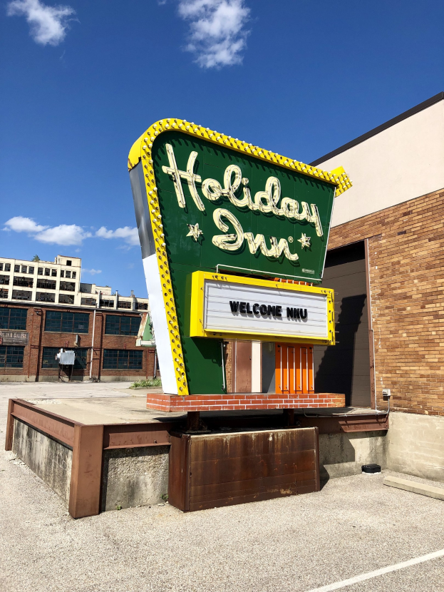 Holiday Inn Schilder auf einem Gebäude mit einem Textboard davor, bewölkter Himmel und sichtbare Fenster im Gebäude.