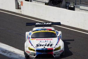 Ein BMW M6 GT3 Rennwagen auf einer Rennstrecke mit einer Wand, einem Maschendrahtzaun und anderen Gegenständen im Hintergrund.