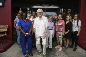 Gruppe von Freiwilligen vor einem Feuerwehrauto mit einer Bank auf der linken Seite und einer Wand im Hintergrund.