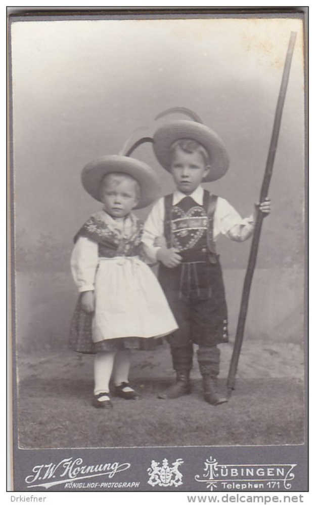 Schwarz-weißes Foto von zwei Kindern in traditioneller bayerischer Tracht, eines hält einen Stock, mit Text unten.