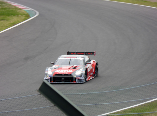 Ein Nissan GT-R Nismo GT3 Rennauto auf der Nürburgring 24 Stunden Strecke, umgeben von grünem Gras auf beiden Seiten.