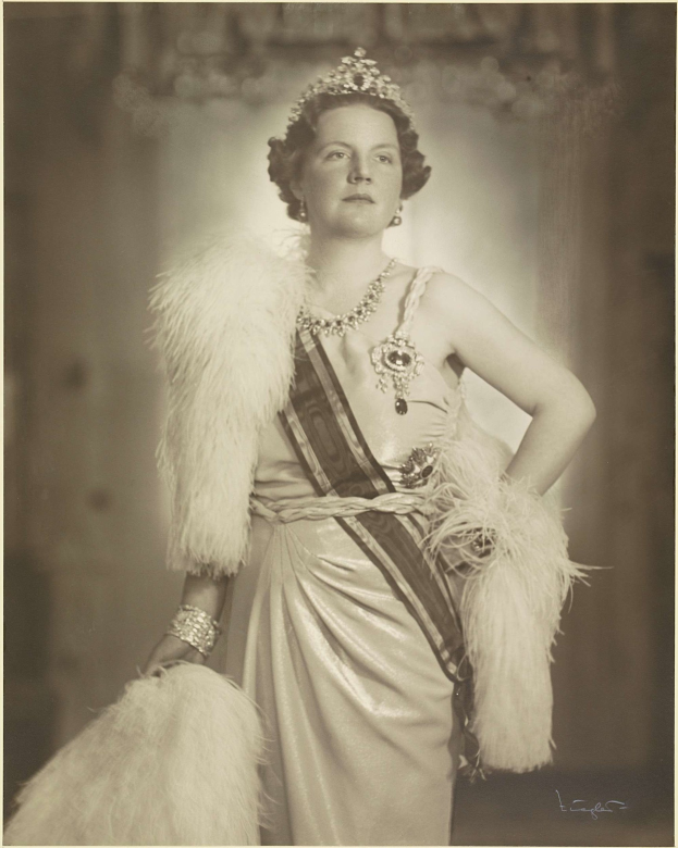 Schwarzes und weißes Foto von Queen Elizabeth II in einem Kleid und einer Krone mit unscharfem Hintergrund und Text unten.