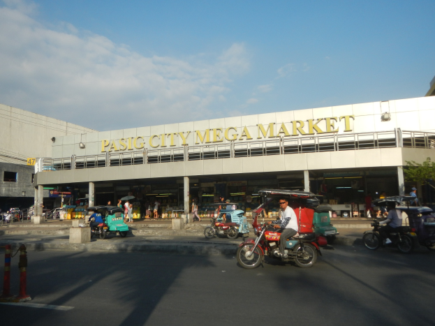 Lebendiger Pasig City Mega Market mit Fahrzeugen auf der Straße, Fußgängern, einem Gebäude mit Text im Hintergrund und einem bewölkten Himmel.