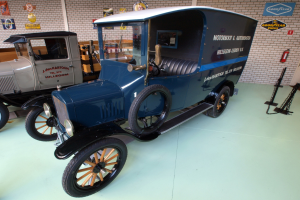 Ein altes Modell-T-Fahrzeug in einem Museum neben anderen Fahrzeugen ausgestellt, mit einem Feuerlöscher und Holzplanken an der benachbarten Wand.
