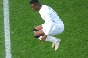 Ein Mann in weißer Uniform kniet auf einem Fussballfeld, mit Fussballstützen.