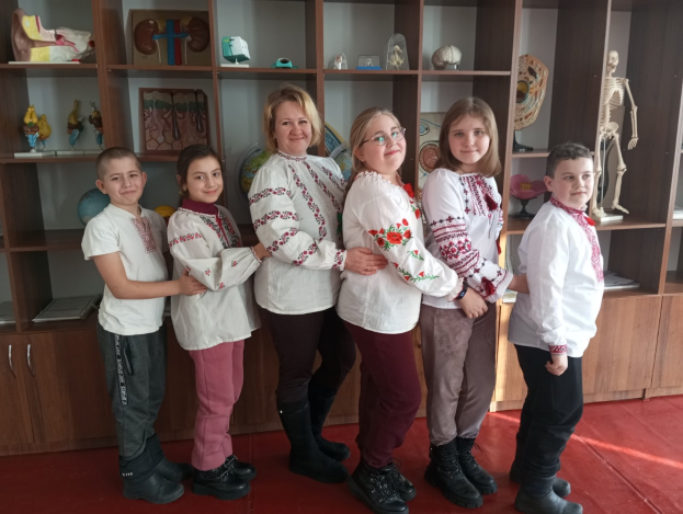 Eine Gruppe von Kindern in traditioneller ukrainischer Kleidung vor einem Regal mit Spielzeug, einem Skelett und anderen Gegenständen