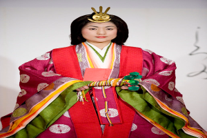 Eine Frau in einem traditionellen japanischen Kimono, die ein leuchtend rotes und grünes Kleid mit aufwändigen Mustern trägt, steht selbstbewusst auf einem Laufsteg mit ihrem Haar zu einem ordentlichen Knoten gebunden.