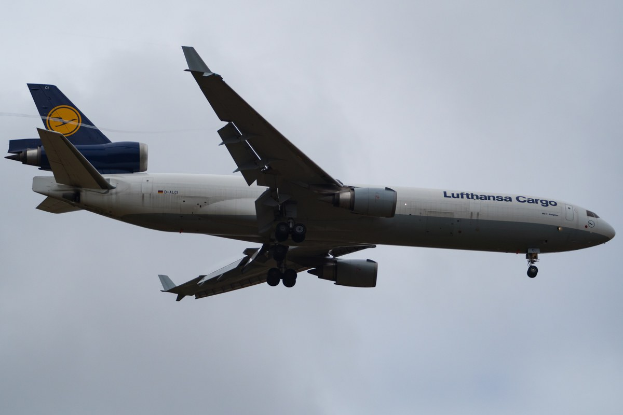 Ein Lufthansa Cargo Boeing 777-300ER im Flug, mit ausgebreiteten Flügeln und laufenden Triebwerken gegen einen teilweise bewölkten Himmel.
