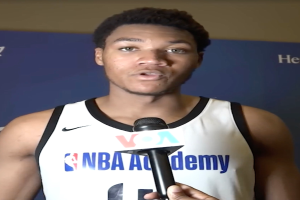 Ein Mann in einem weißer Tanktop hält ein Mikrofon und steht vor einer Tafel, auf der "NBA All-Star Game 2019" steht, und einer Wand, wahrscheinlich spricht er mit den Medien.